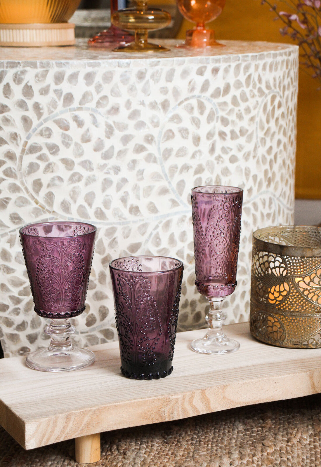 Purple glassware on a wooden surface with a textured wall in the background