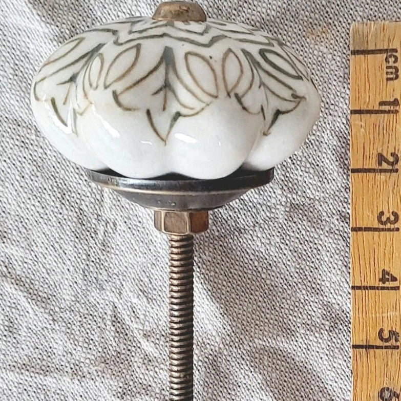 Decorative ceramic knob with floral patterns on a textured surface next to a wooden ruler.