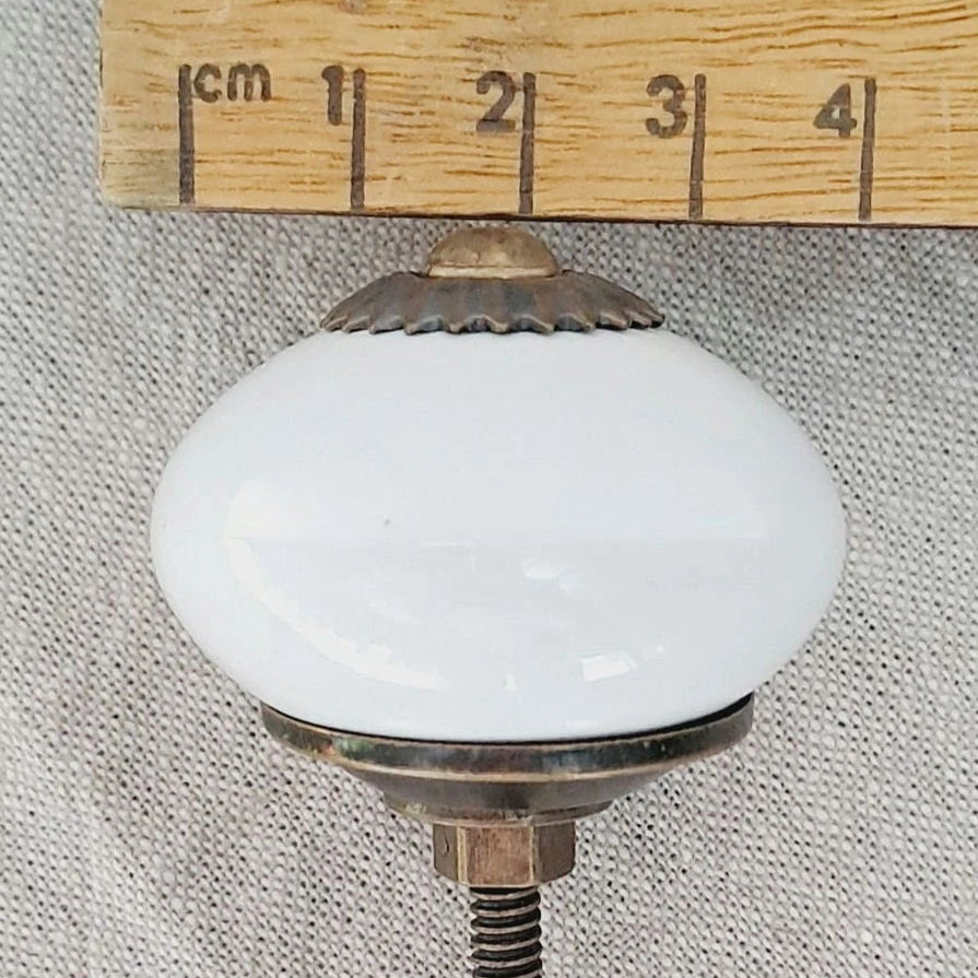 Vintage-style light bulb with white glass and brass base, measured against a wooden ruler.
