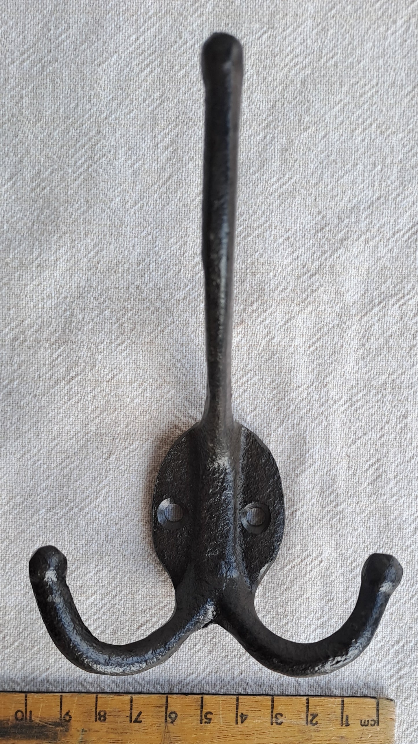 Black metal double hook with a ruler for scale on a gray background