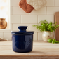 Blue butter container on a kitchen counter with a tiled wall and wooden cutting board in the background.