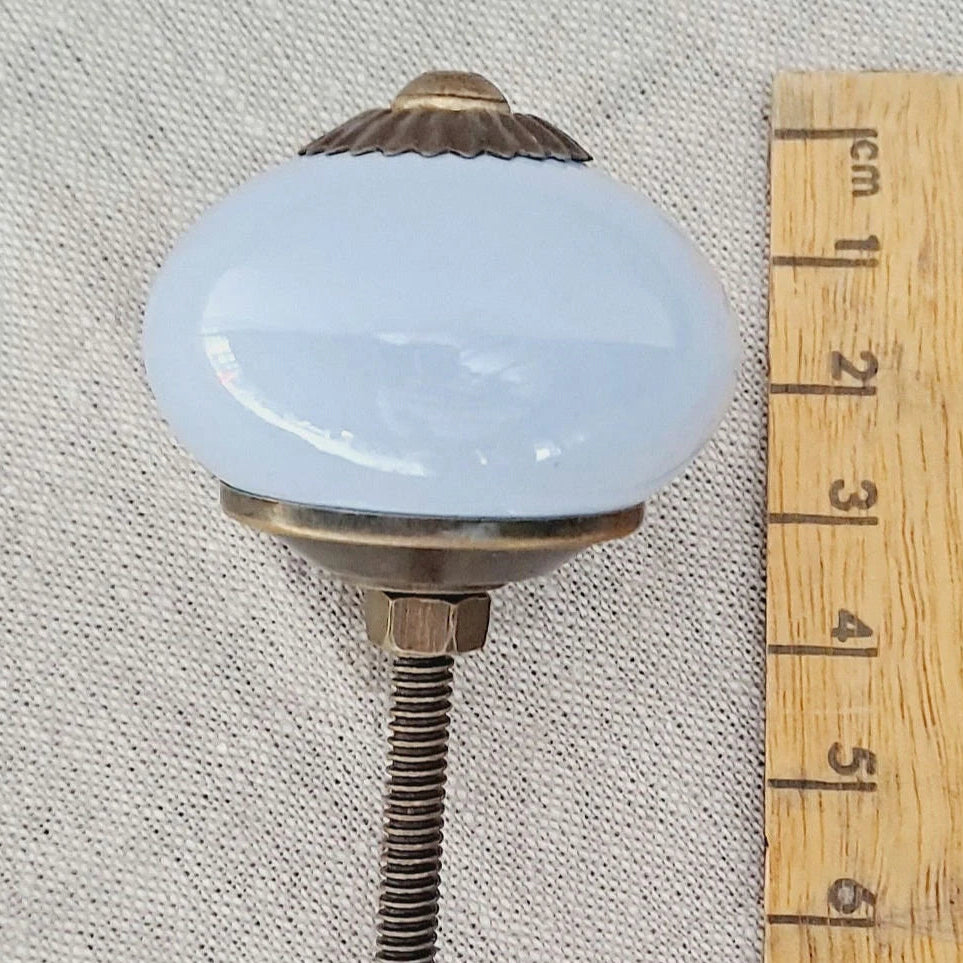 Decorative knob with a light blue glass ball and brass accents, next to a wooden ruler for scale.