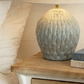 Decorative lamp on a bedside table with a textured design, next to a blanket and books.