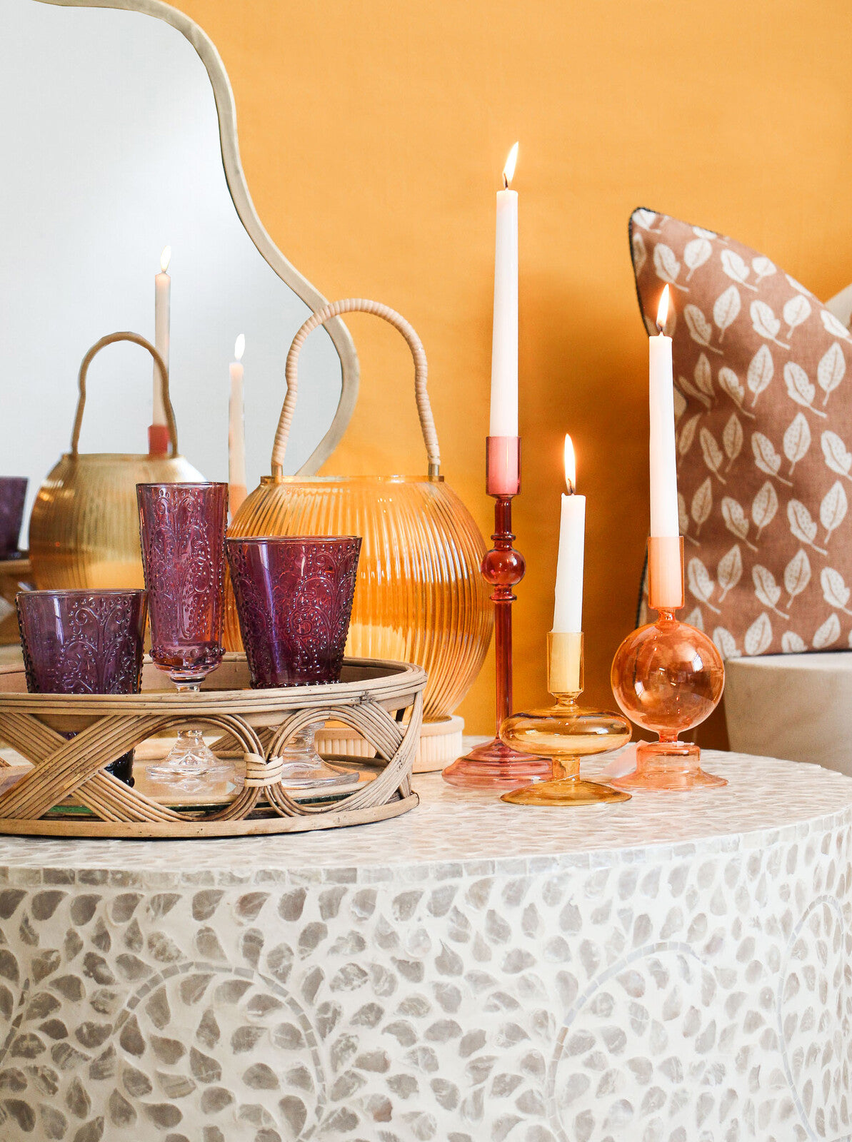 Decorative table setting with candles, glasses, and a mirror against an orange wall.