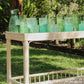 Green glassware on a wooden table outdoors with greenery in the background