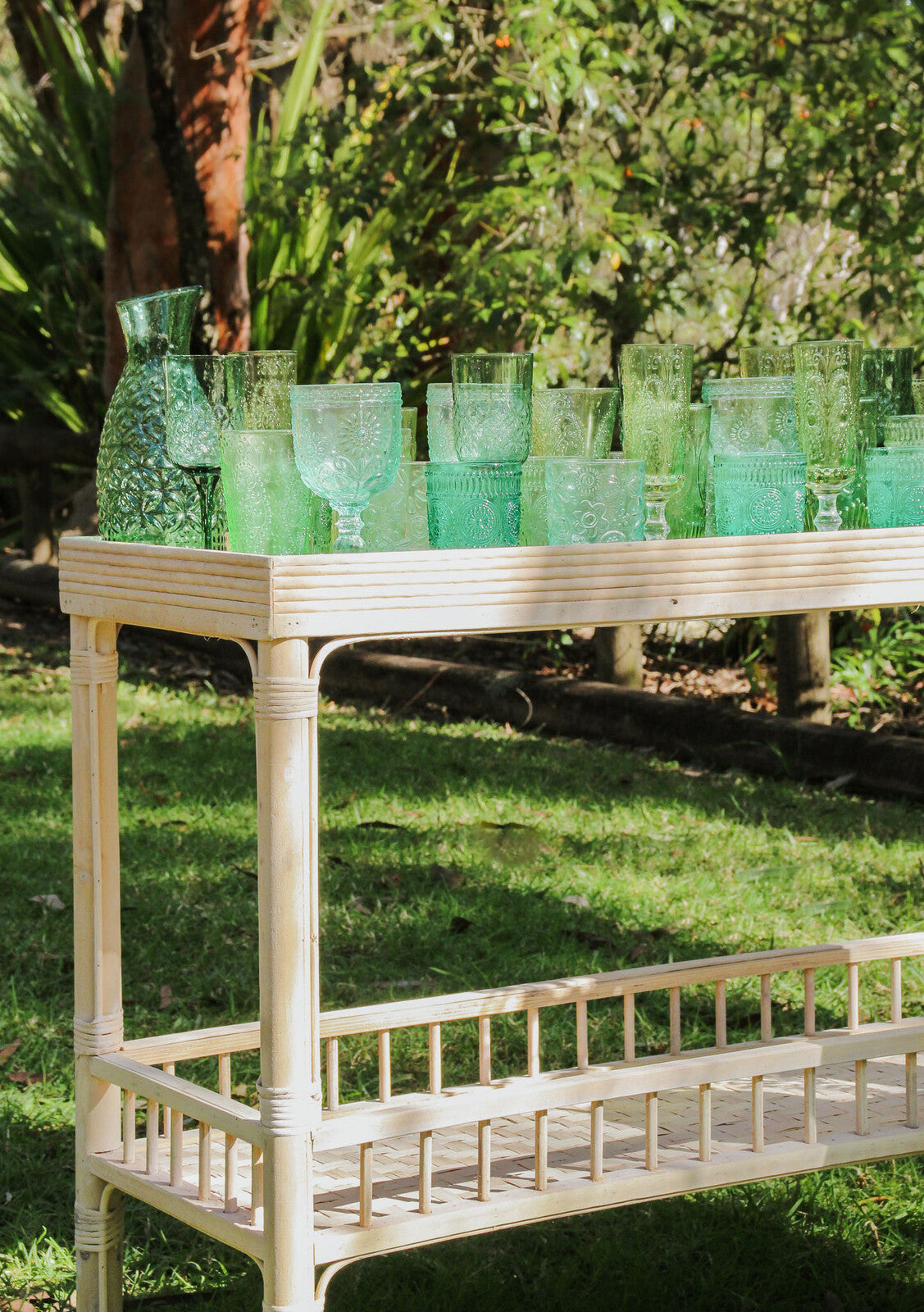 Green glassware on a wooden table outdoors with greenery in the background