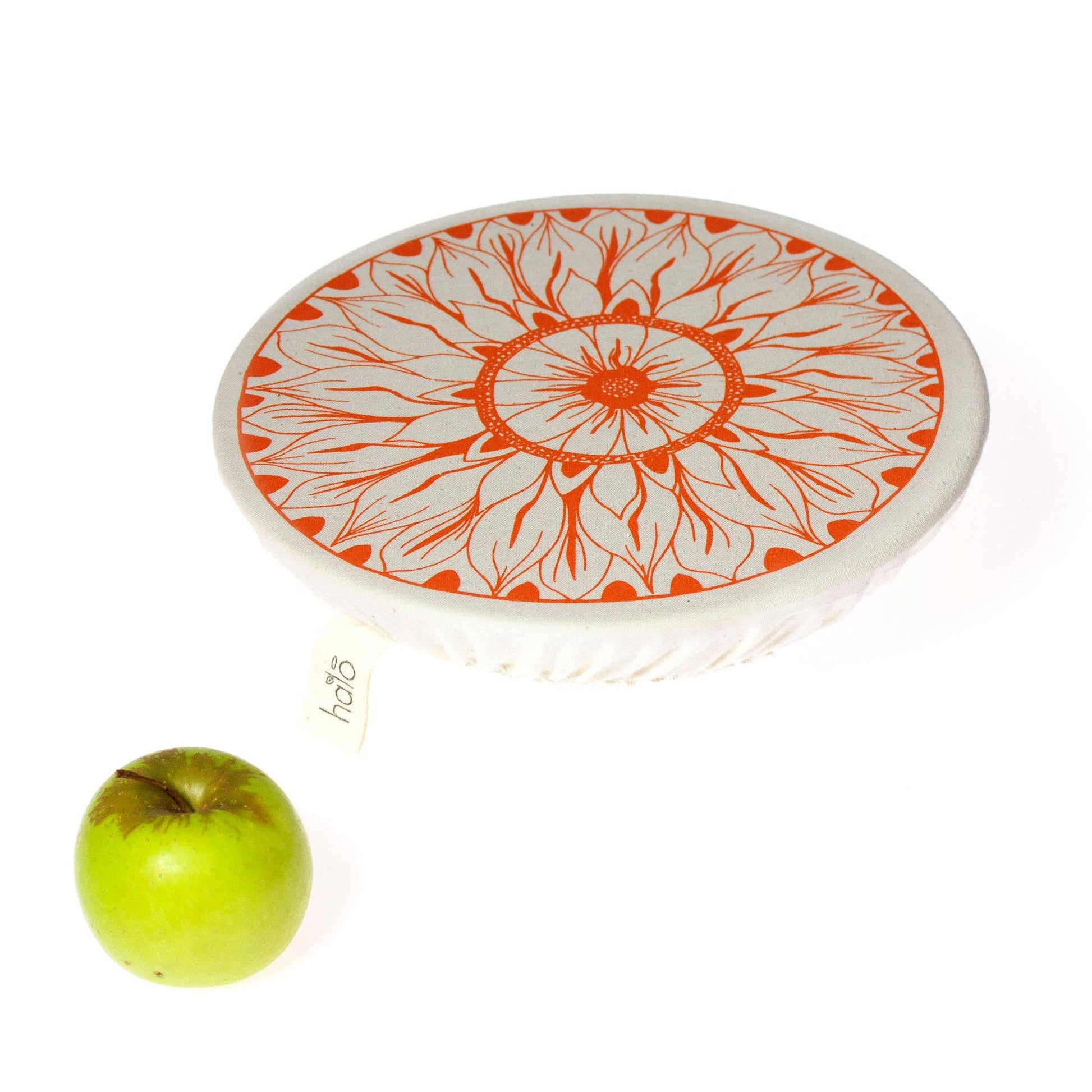 Round white plate with orange floral pattern next to a green apple on a white background