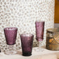 Purple glassware on a wooden surface with a textured wall in the background