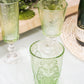 Green patterned glasses on a white surface with a bottle in the background