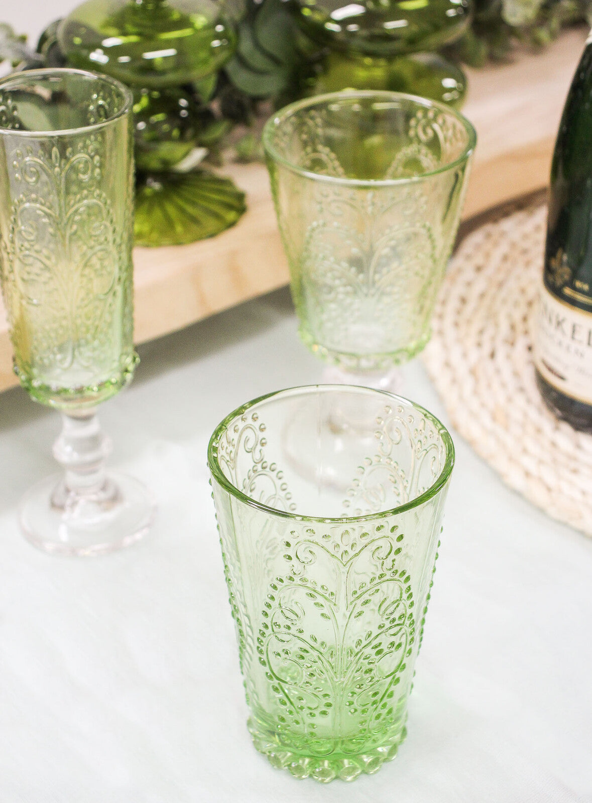 Green patterned glasses on a white surface with a bottle in the background