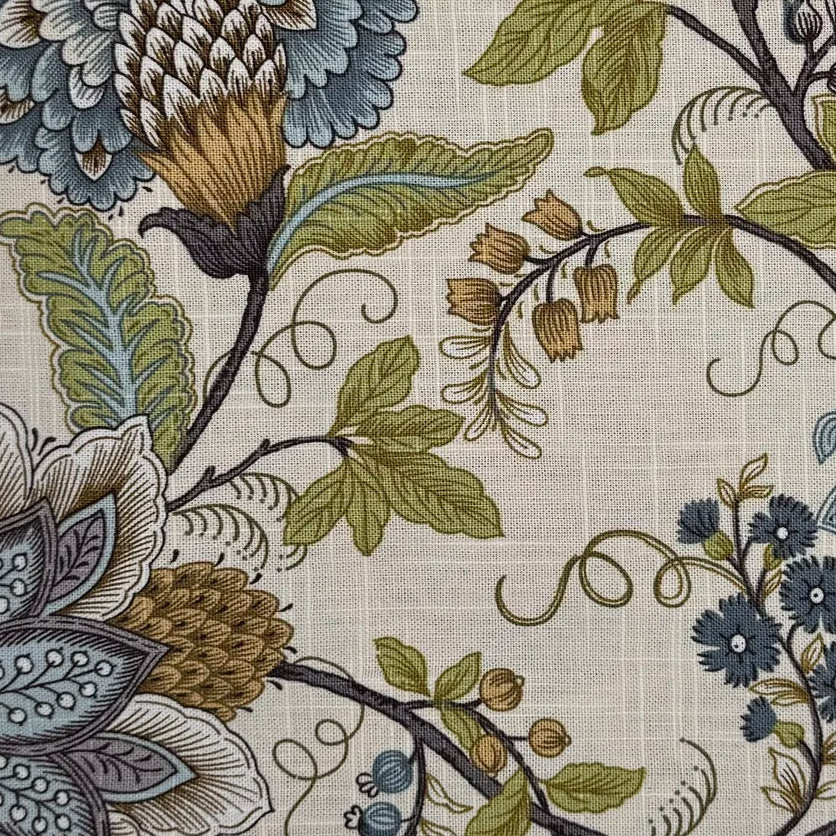 A close-up of a floral fabric pattern on a textured beige linen-like background, featuring blue-gray, olive green, mustard yellow, and dark brown botanical motifs.