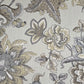 A close-up of a floral fabric pattern featuring large peony-like flowers and leaves in muted beige, gray, and taupe tones on a light warm gray background.