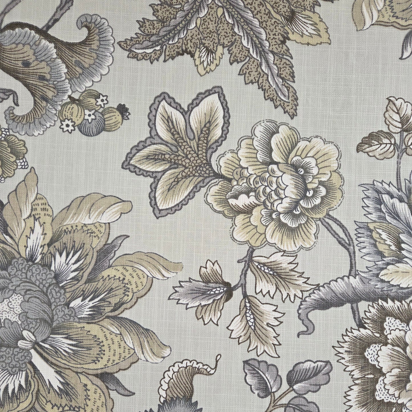 A close-up of a floral fabric pattern featuring large peony-like flowers and leaves in muted beige, gray, and taupe tones on a light warm gray background.