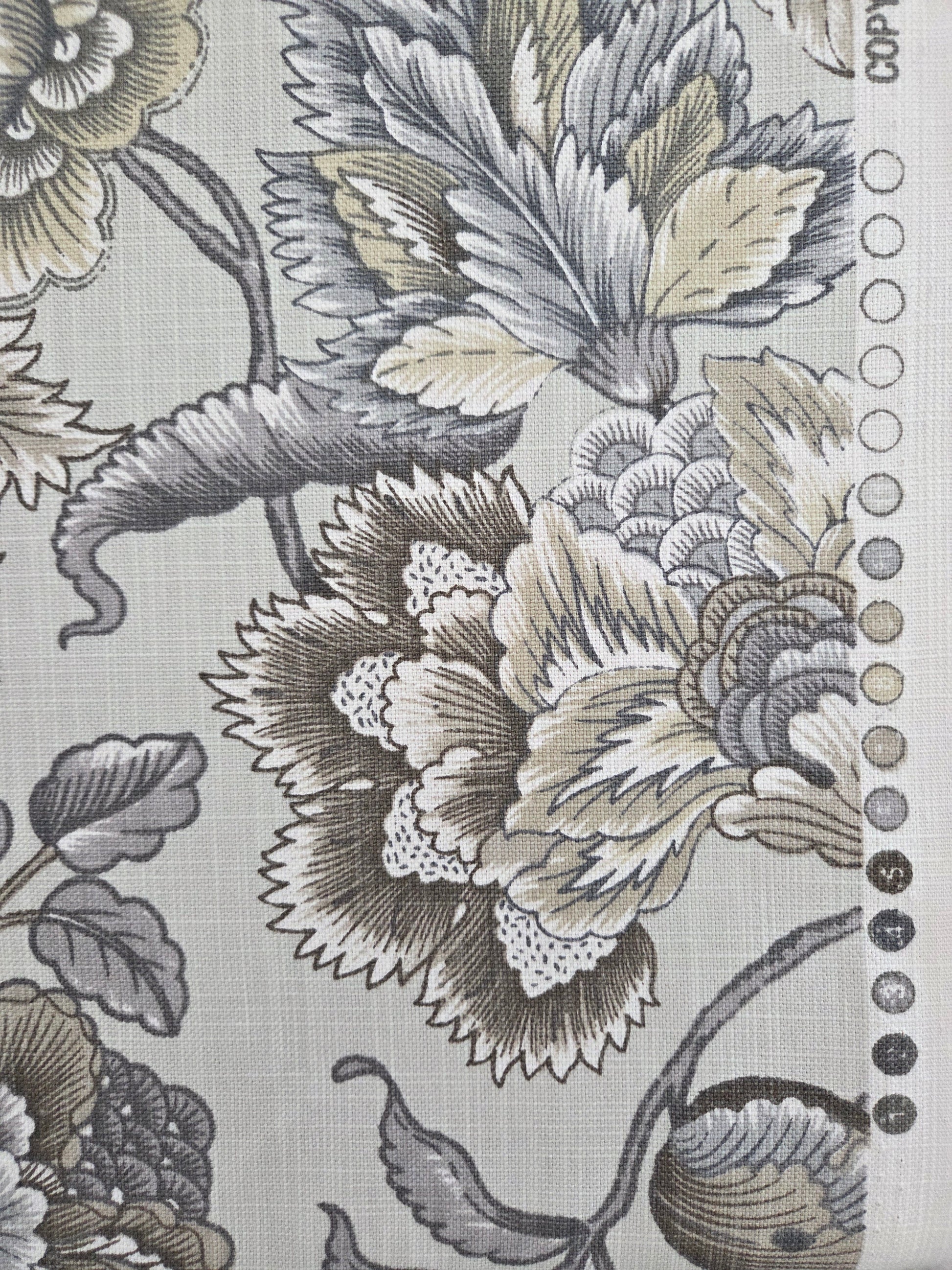 A close-up of a fabric or wallpaper pattern featuring large floral motifs in gray, beige, and black on a light gray background, with a row of small circular color swatches along the top edge.
